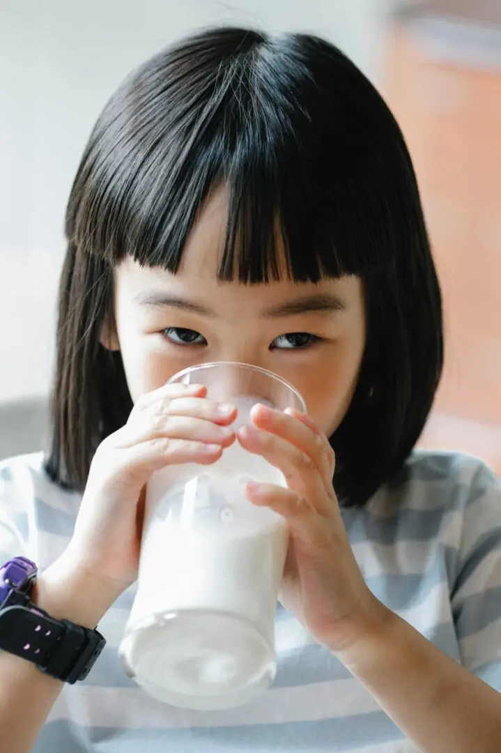 A little girl drinking milk from a glass.