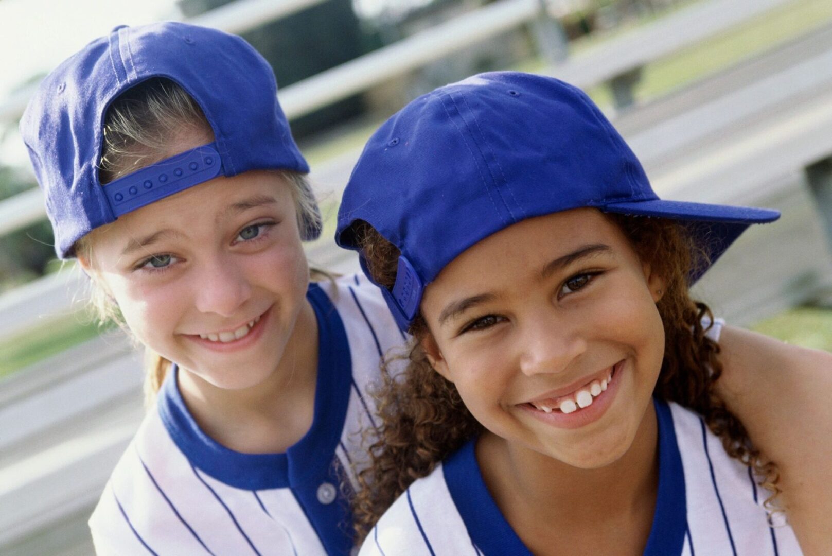 Two young girls in baseball uniforms and hats.