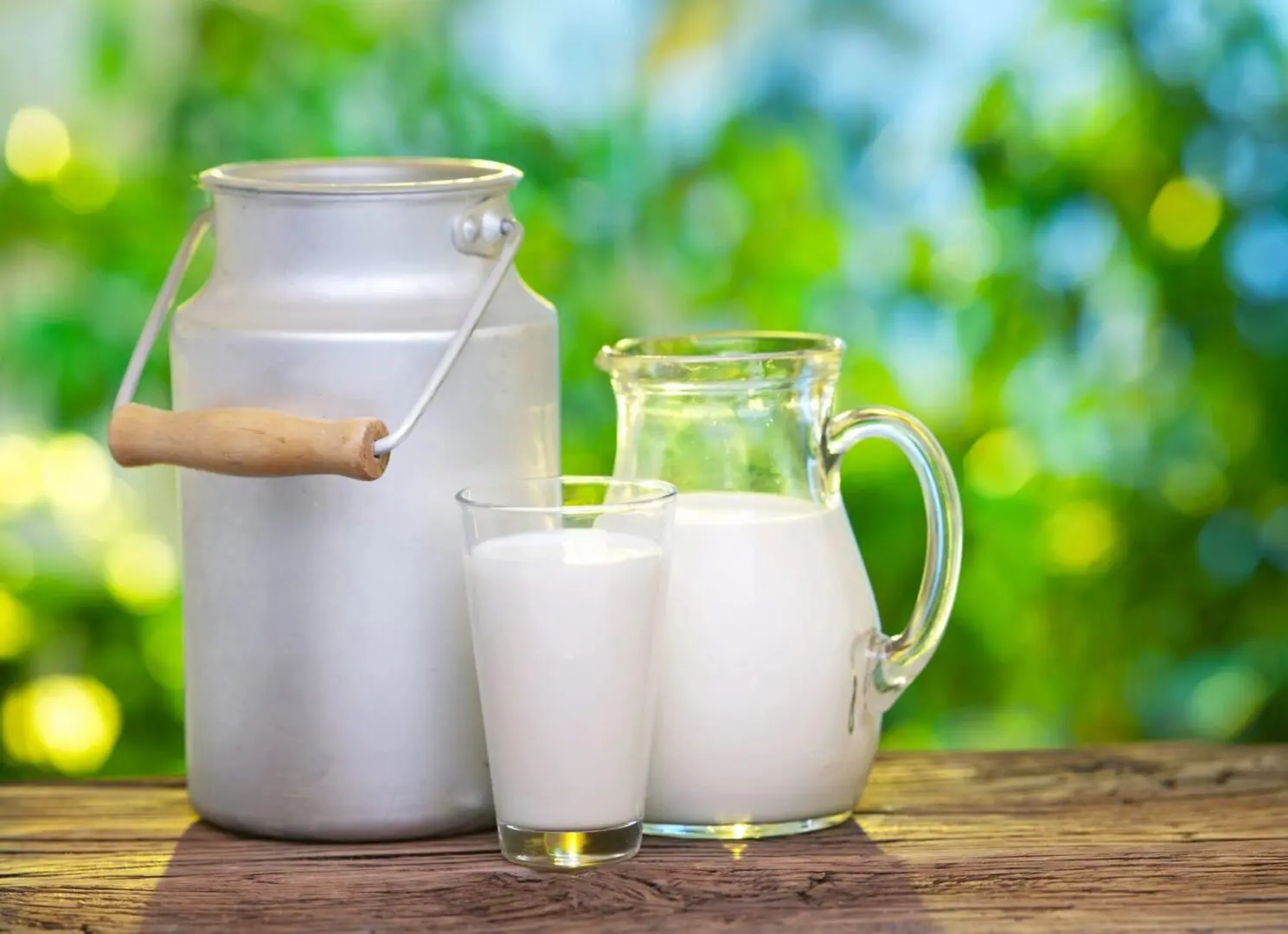 A pitcher and two glasses of milk on a table.