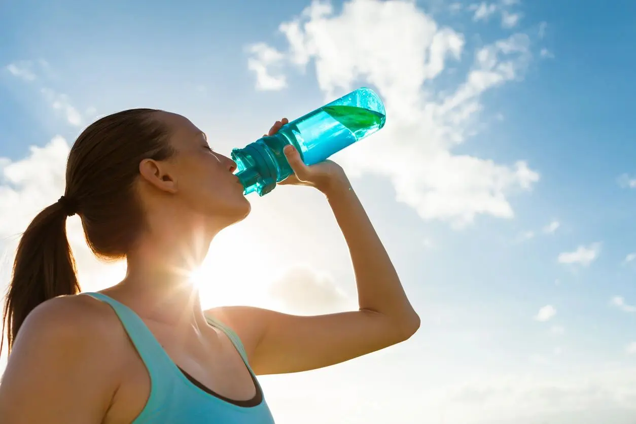 A woman drinking water from a blue bottle.